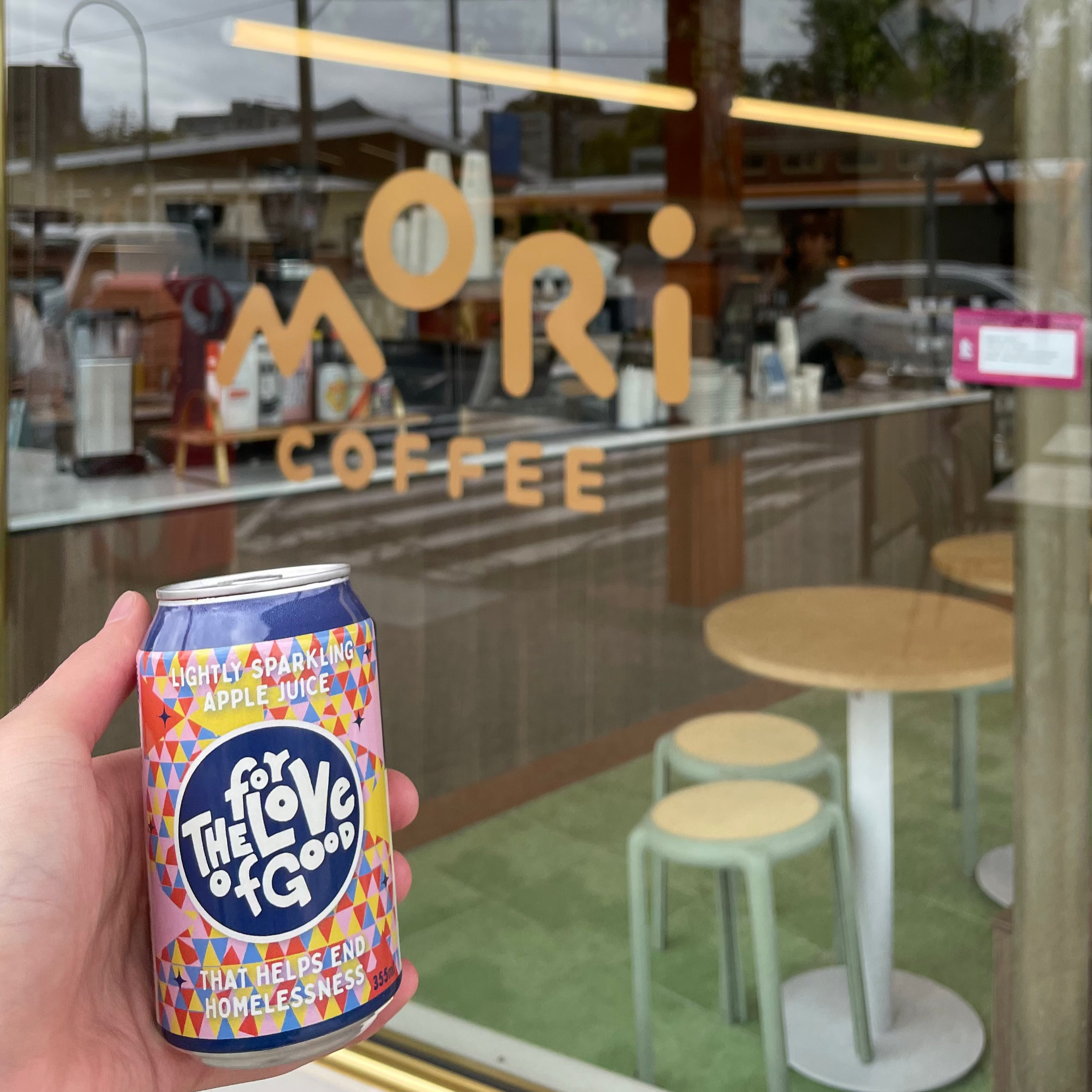 Hand holding a colorful can in front of a glass door with 'Mori Coffee' sign.